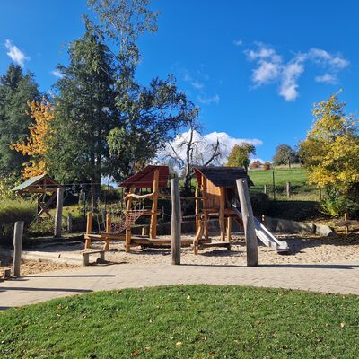 Spielplatz mit h&ouml;lzernen Klettereinrichtungen, blauer Himmel, im Hintergrund B&auml;ume