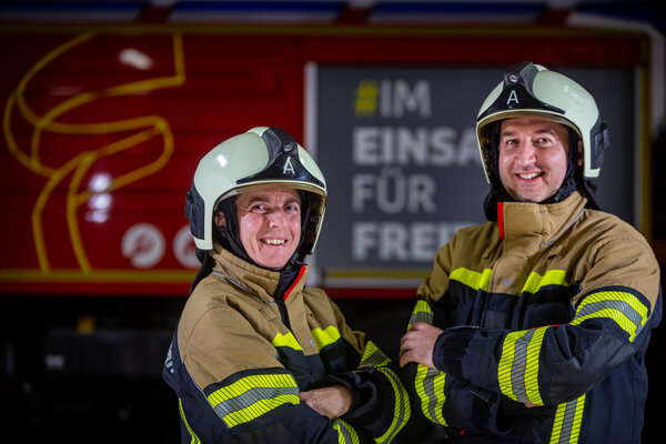 Eine Frau und ein Mann in Feuerwehrmontur vor einem Einsatzfahrzeug