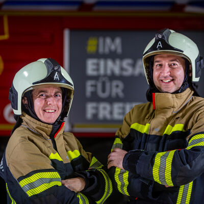 Eine Frau und ein Mann in Feuerwehrmontur vor einem Einsatzfahrzeug
