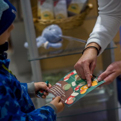 Ein Kind h&auml;lt einen Flyer mit Stiefeln darauf in der Hand. Ein Erwachsener zeigt dem Kind, wo Aufkleber platziert werden m&uuml;ssen, um einen Preis zu erhalten.