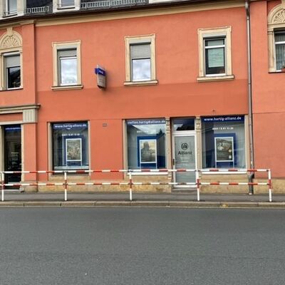 Im Erdgeschoss eines gro&szlig;en Eckhauses befindet sich ein Schaufenster. Darin h&auml;ngt Werbung der Allianz.