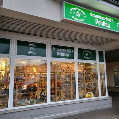 In einer H&auml;userfassade befindet sich ein Schaufenster. Im Schaufenster stehen Pyramiden, Schwibb&ouml;gen und andere weihnachtliche Dekoration. &Uuml;ber dem Gesch&auml;ft h&auml;ngt ein Werbeschild.